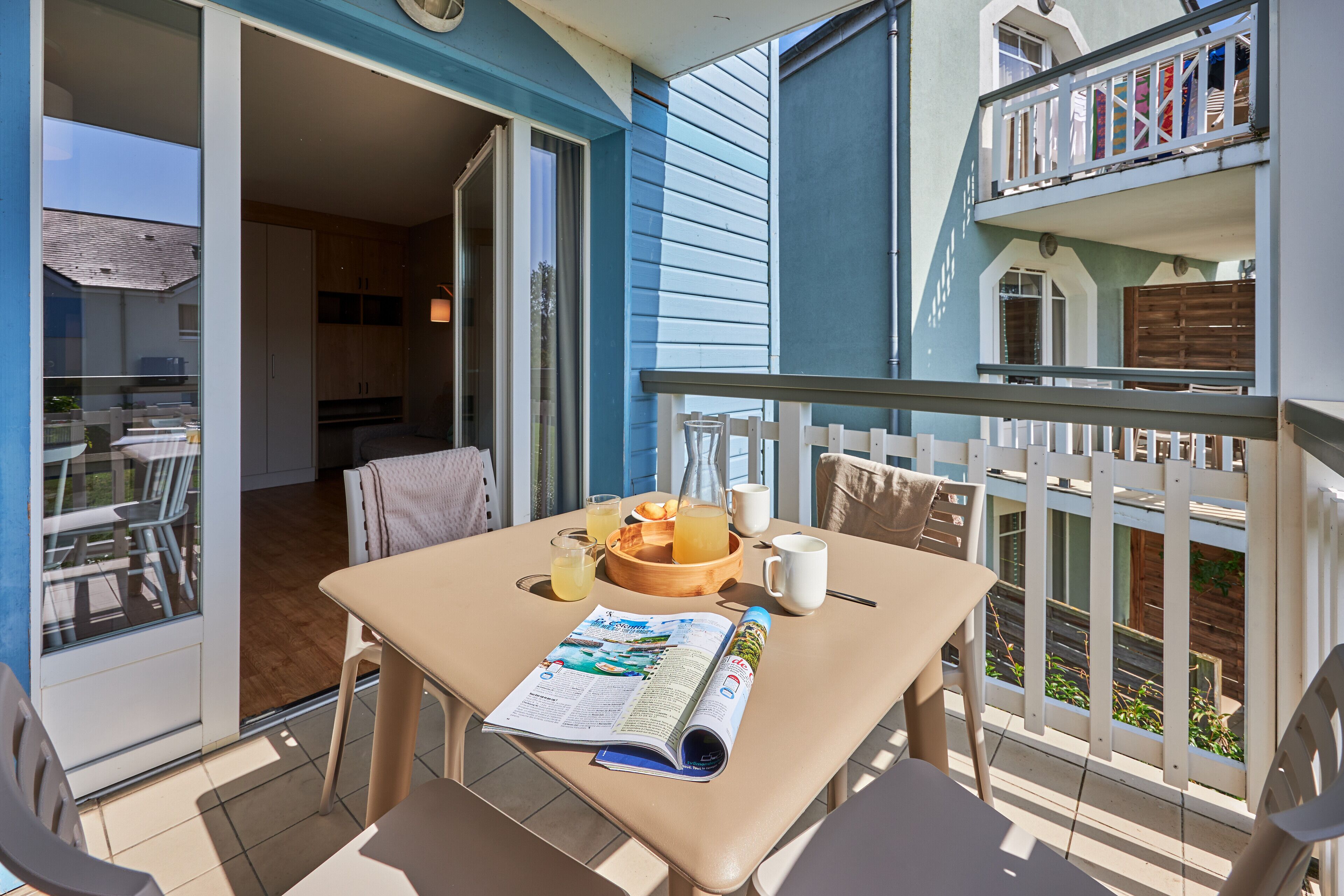 A balcony with a table set for breakfast, including a magazine, a bowl of fruit, and a cup of coffee.