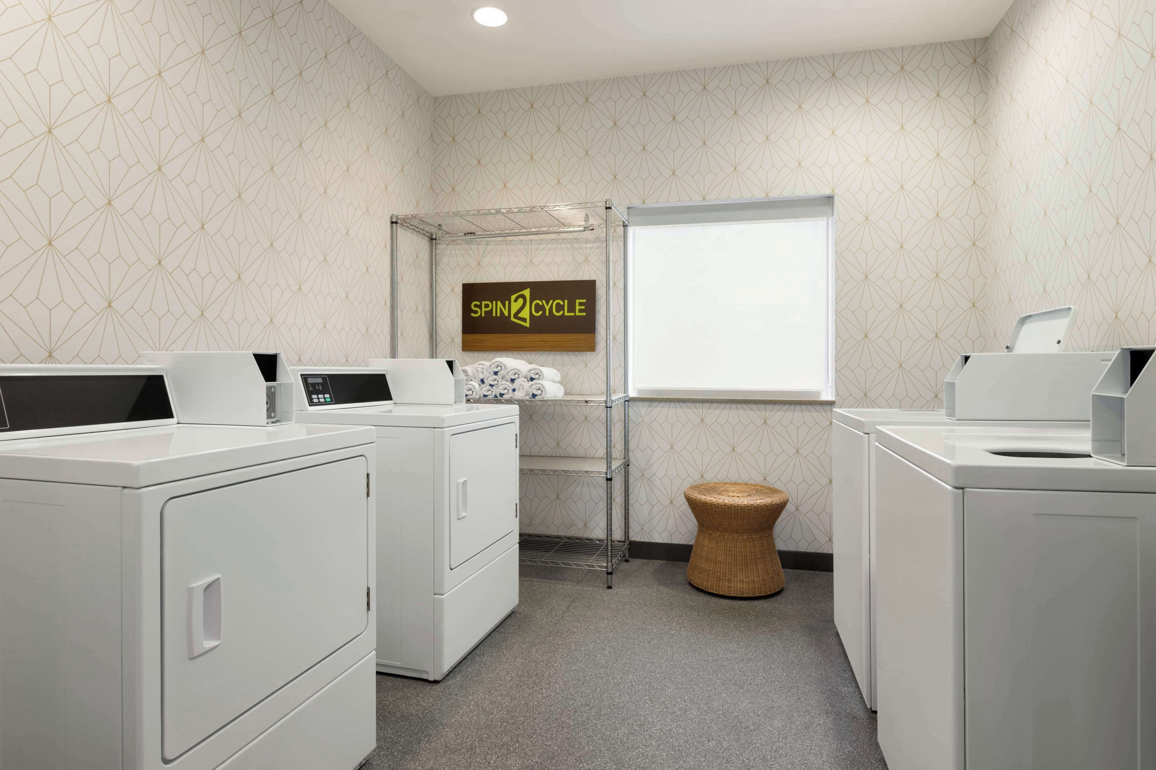 A laundry room with white appliances, a sign reading "SPIN2CYCLE," and a window.