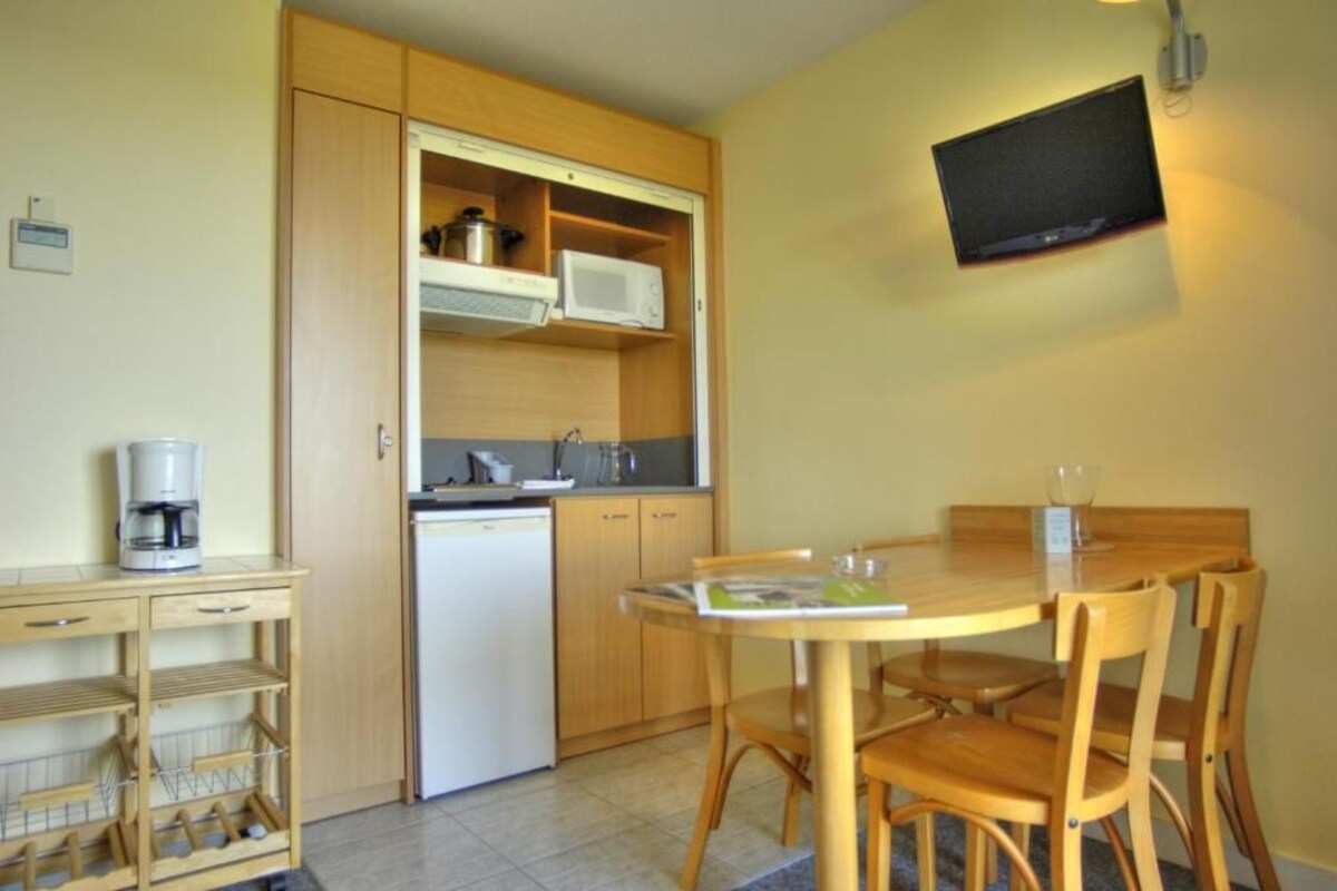 A compact kitchen with wooden cabinets, a microwave, a coffee maker, and a small dining table with chairs.