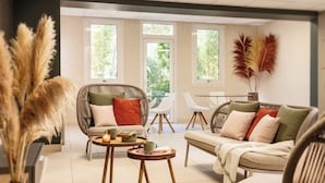 A modern living room with a sofa, chairs, and a coffee table. There are large windows and a view of greenery outside.