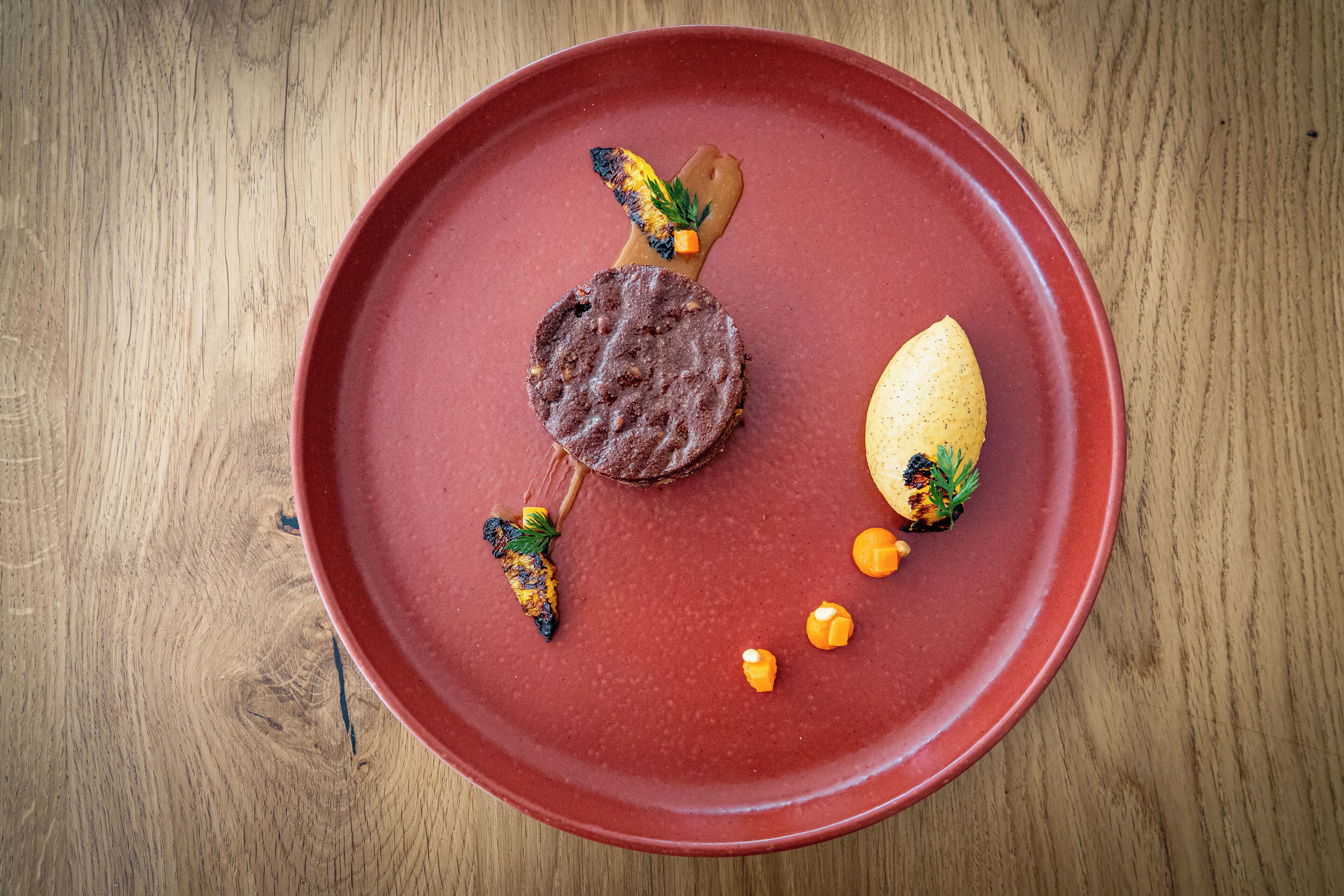 A red plate with a meat dish, a grilled vegetable, and a piece of bread.