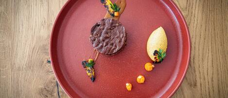 A red plate with a meat dish, a grilled vegetable, and a piece of bread.