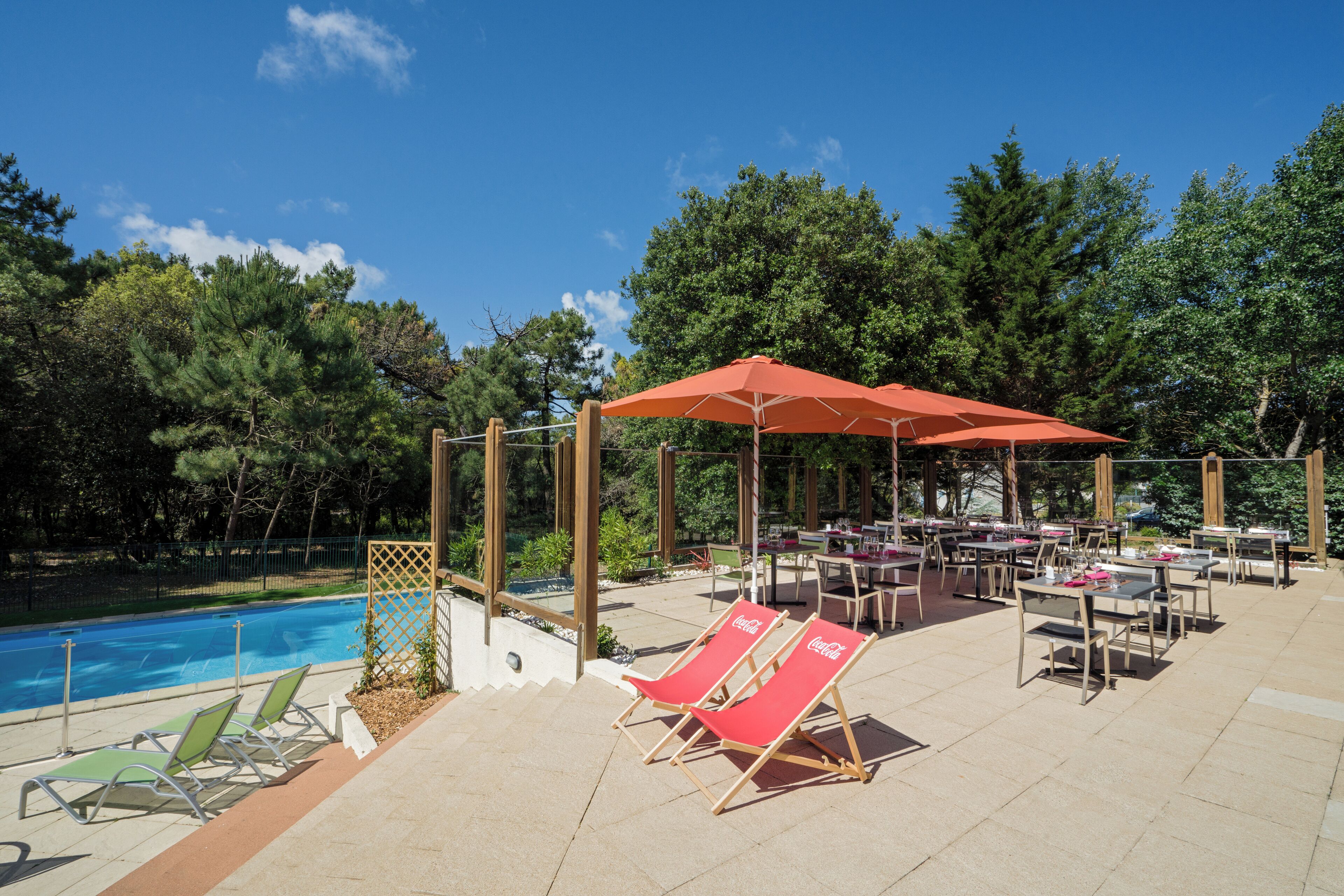 Un espace aménagé au bord de la piscine, avec des chaises longues et des parasols, entouré d’arbres et donnant sur la piscine.