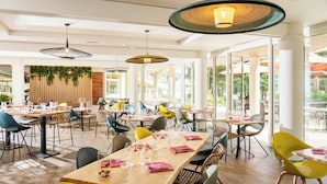 A spacious dining area with multiple tables and chairs, large windows, and hanging pendant lights.