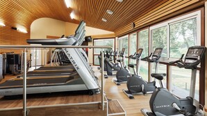 A gym with treadmills, elliptical machines, and exercise bikes, featuring wooden ceilings and large windows.