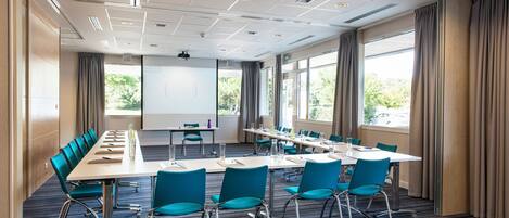 A conference room with a long table, blue chairs, and large windows.
