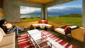 Un intérieur moderne avec une grande fenêtre donnant sur un lac et des montagnes.