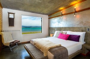 A bedroom with a large bed, a view of the sea, a chair, and a window.
