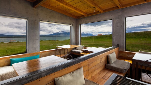 Un intérieur moderne avec de grandes fenêtres, des poutres en bois et une vue sur les montagnes et l’eau.