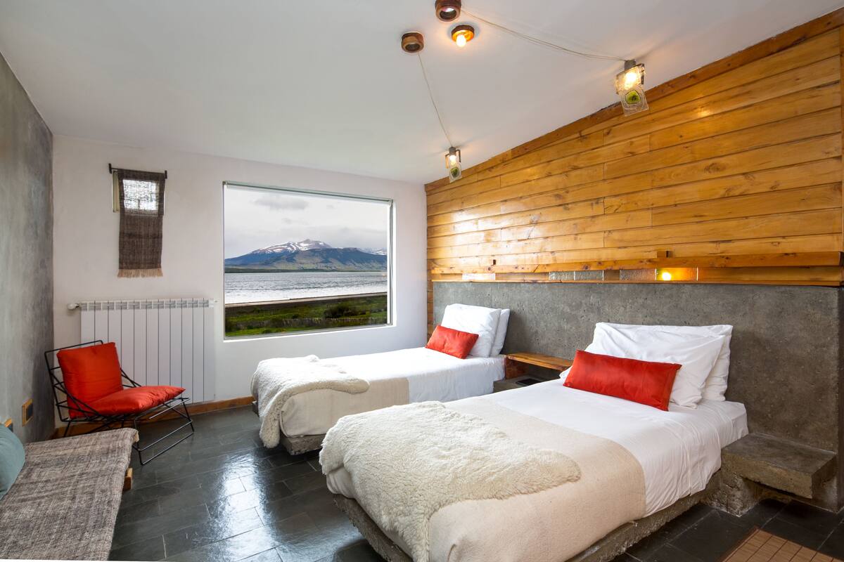 Una habitación con dos camas, una silla roja, vistas a las montañas y paneles de madera en la pared.