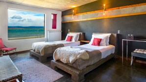 Une chambre avec deux lits, une vue sur la mer et une grande fenêtre.