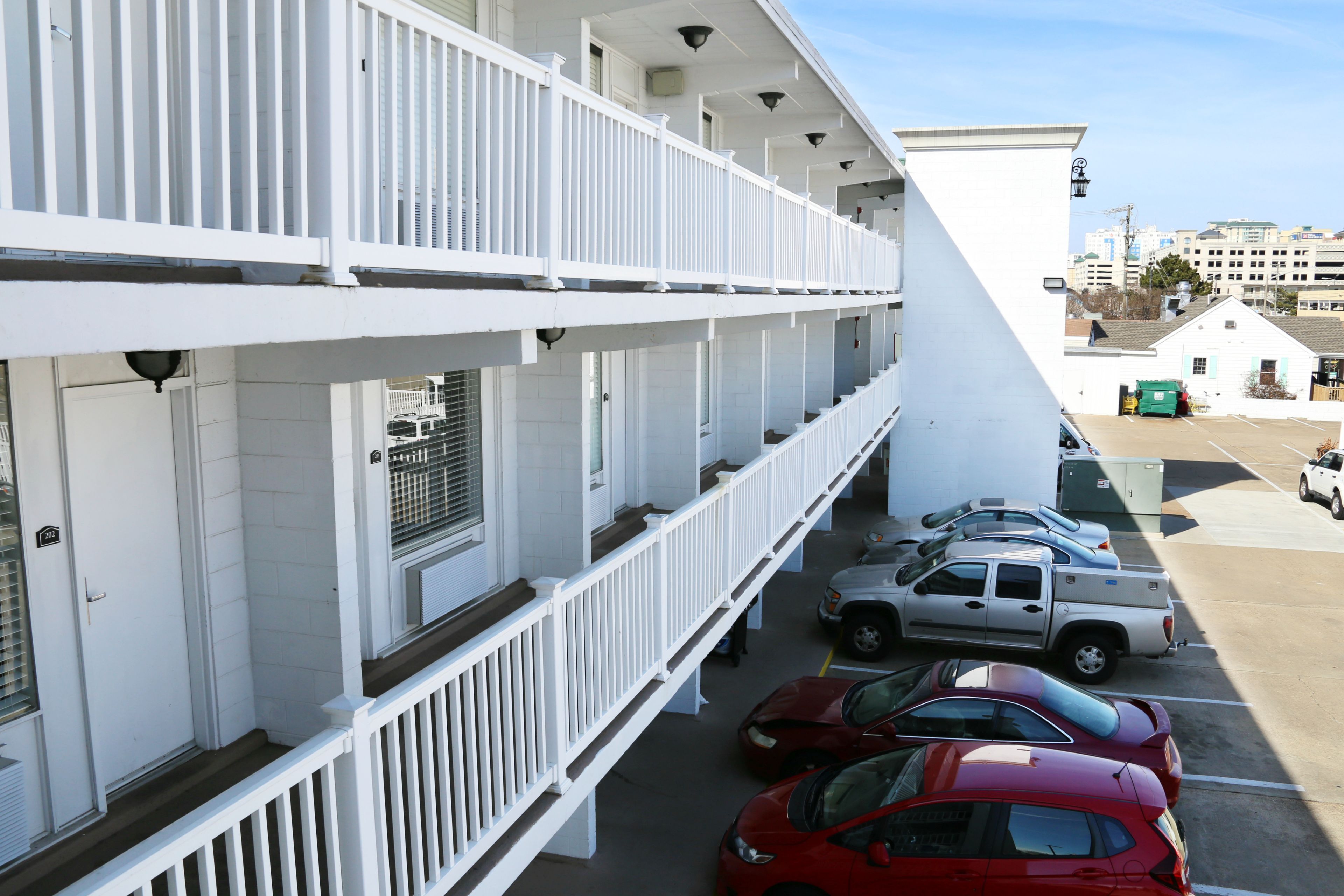 A multi-story building with white railings and a parking area with several cars.