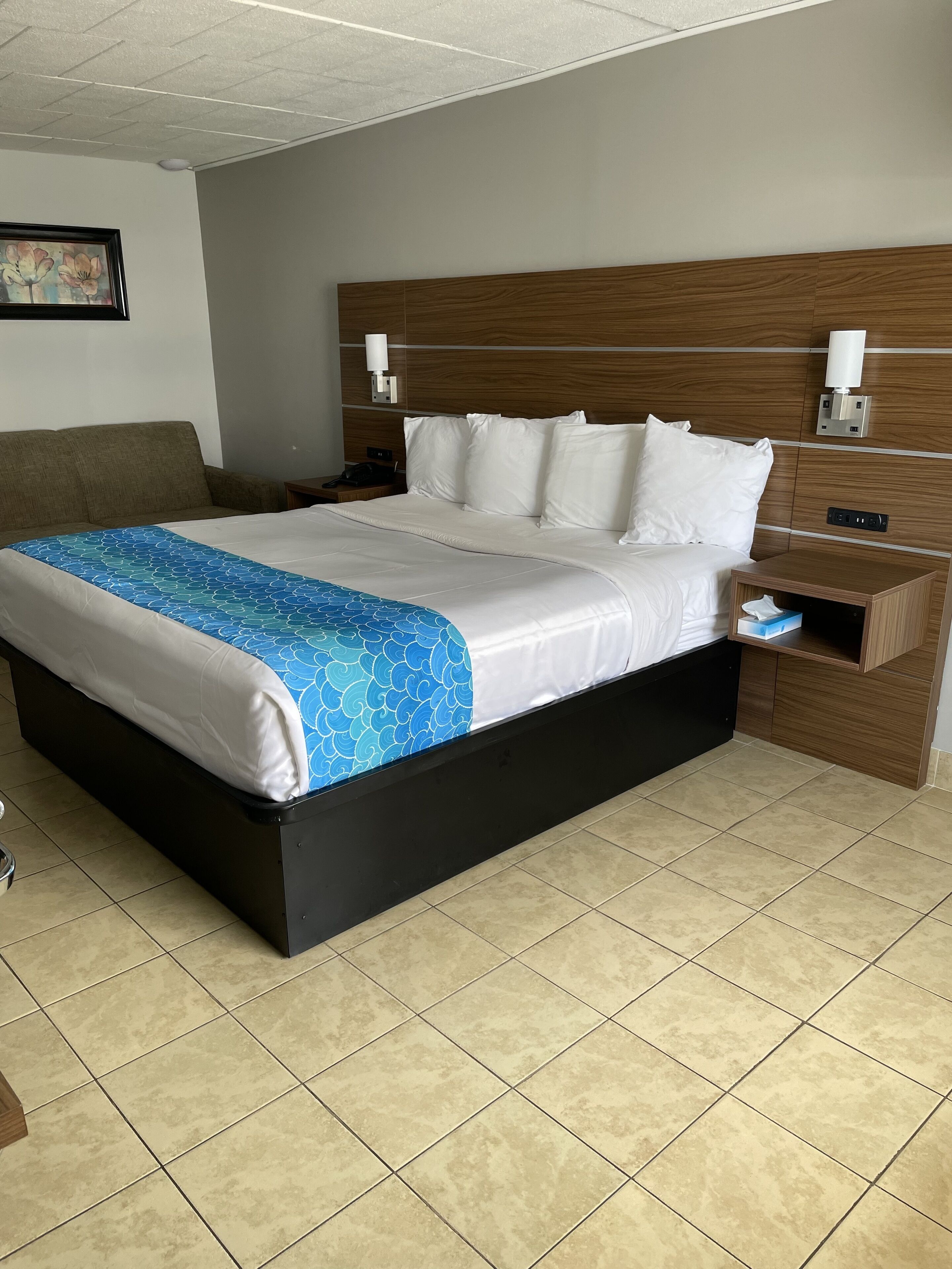 A hotel room with a large bed, a wooden headboard, a nightstand, and a wall-mounted lamp.