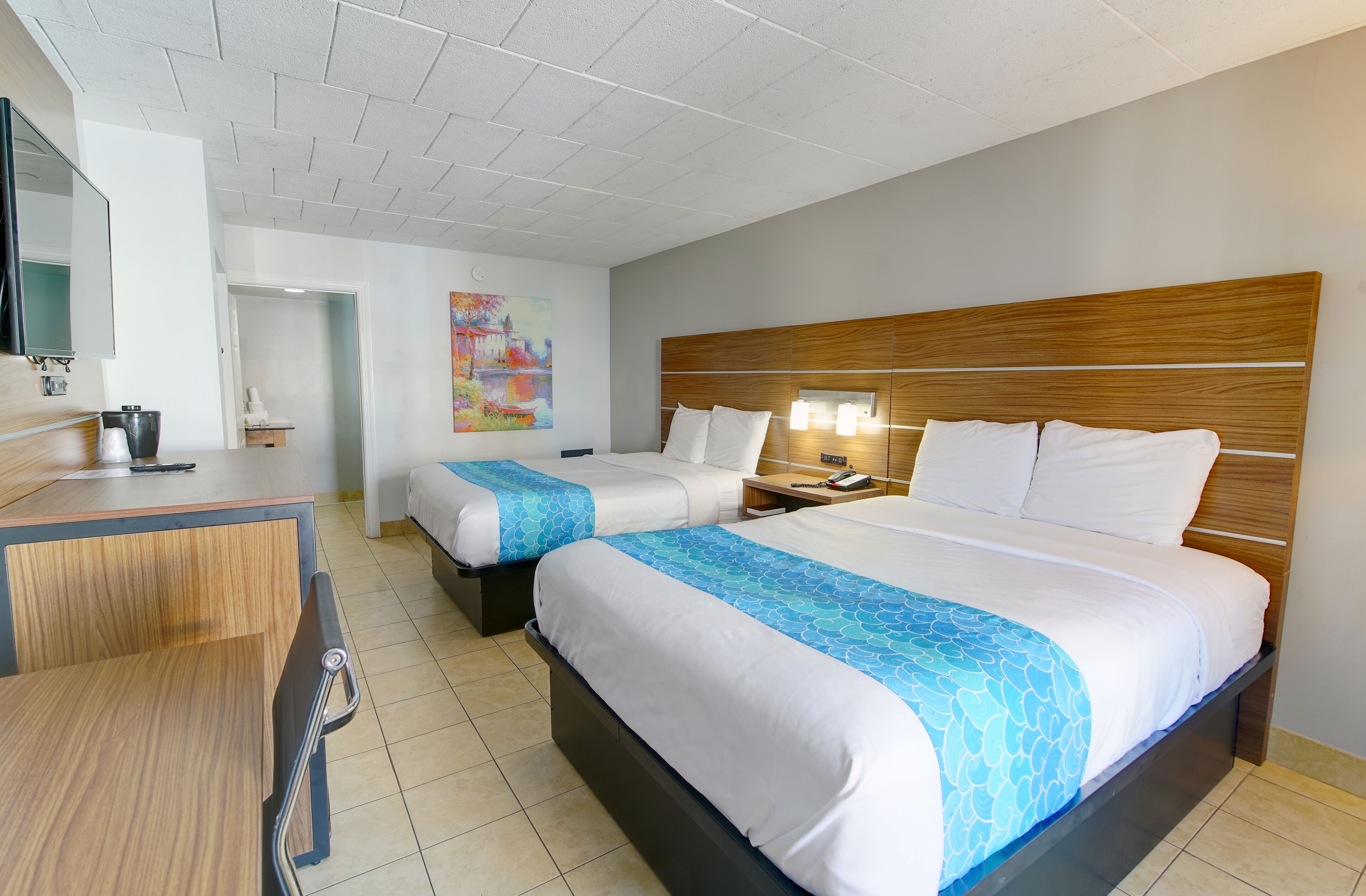 A hotel room with two beds, a desk, and a mirror.