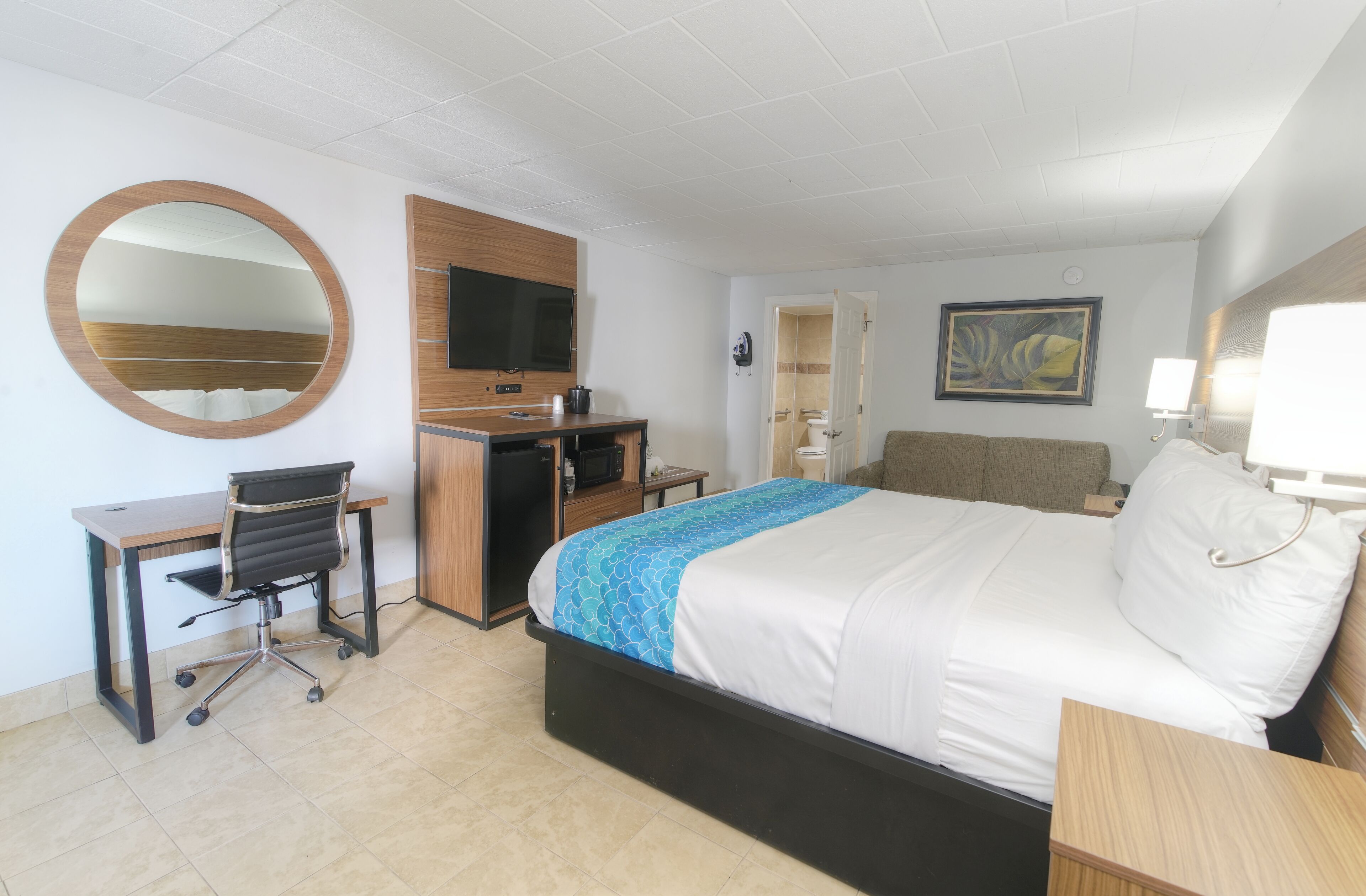 Ein Hotelzimmer mit Bett, Schreibtisch, Sessel, Fernseher und einem Bild an der Wand.