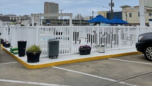 Un estacionamiento con cerca blanca, plantas en macetas y un toldo azul.