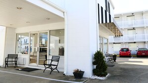 Un edificio con fachada blanca, entrada de vidrio y un estacionamiento con dos autos.