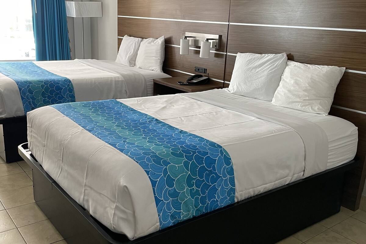 A hotel room with two beds, a nightstand, and a wall-mounted lamp.