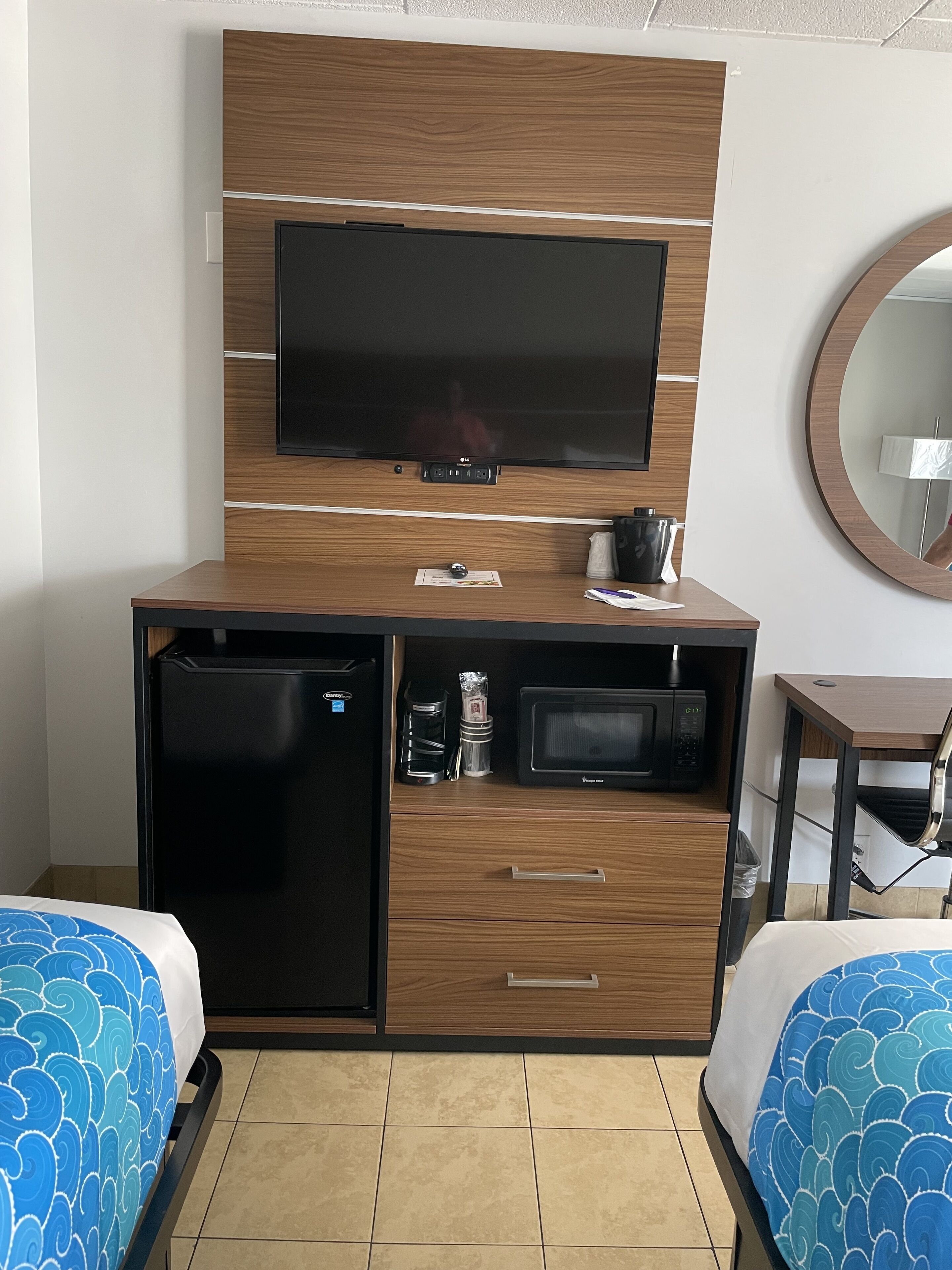 A hotel room with a bed, a small refrigerator, a microwave, a coffee maker, and a television on a wooden cabinet.