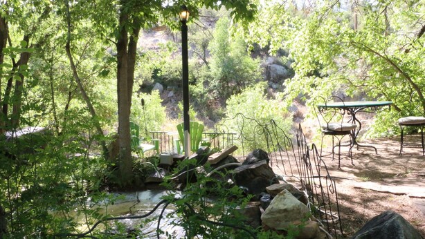 A serene outdoor setting with a small stream, picnic tables, and a metal fence. - Apple Creek Cottages (Prescott)