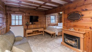 A cozy log cabin interior with a fireplace, wooden furniture, and a television. - Apple Creek Cottages (Prescott)