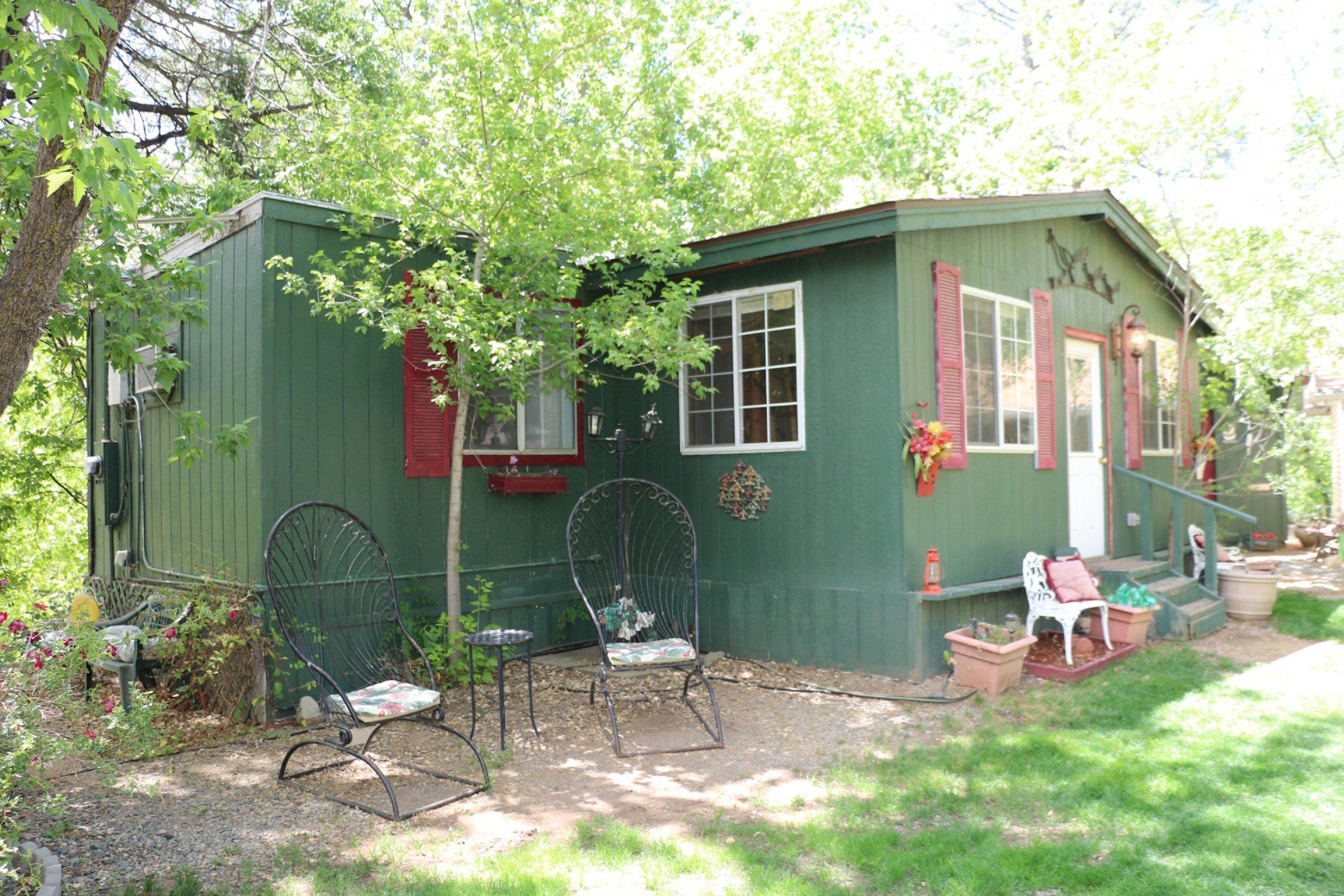 A small green building with a porch, two rocking chairs, and a white chair.