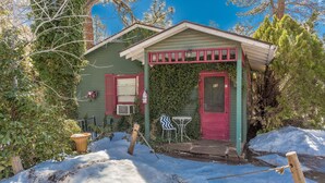 A small, green building with a red door and window shutters, surrounded by snow and trees. - Apple Creek Cottages (Prescott)