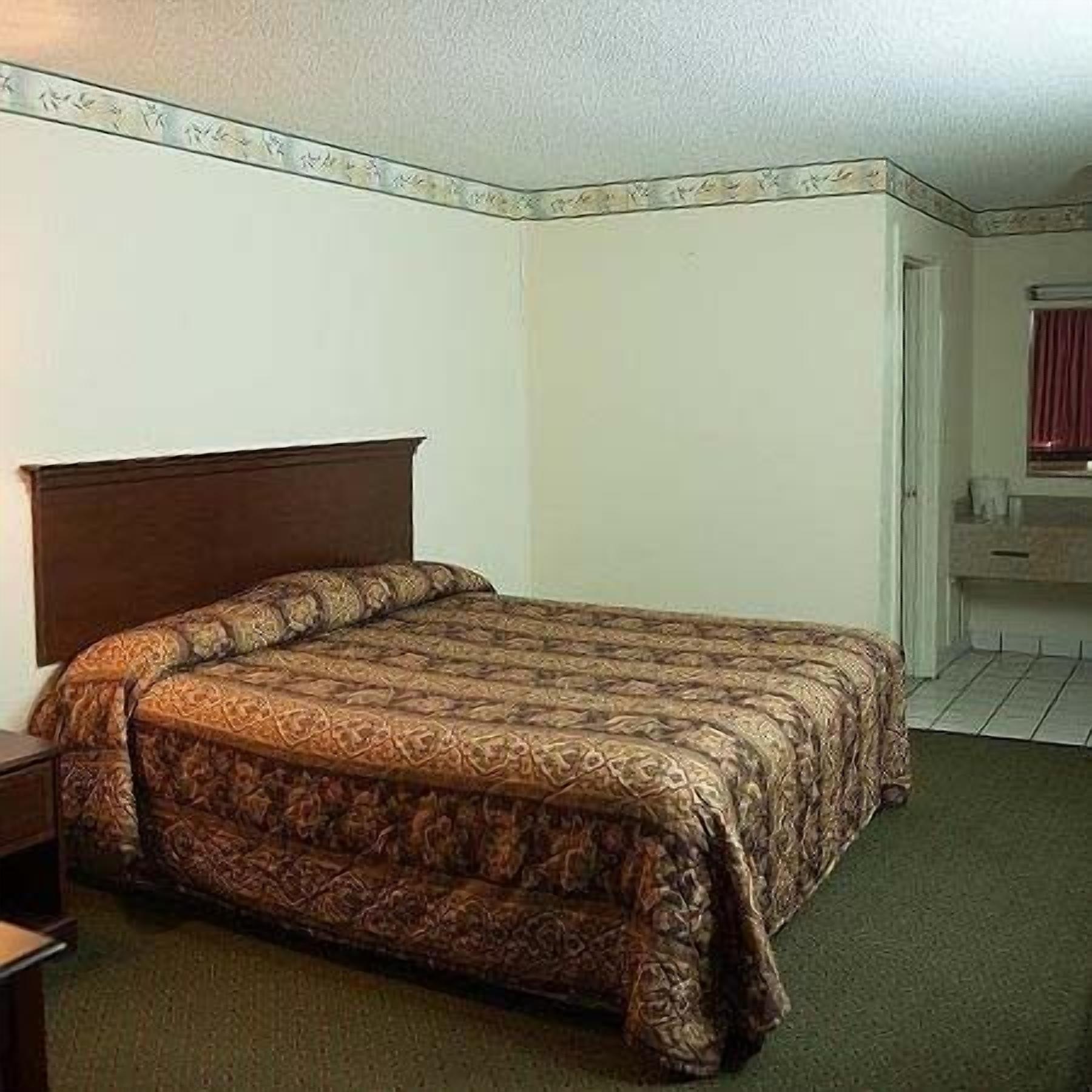 A standard hotel room with a single bed, a nightstand, a dresser, and a bathroom with a mirror and sink.
