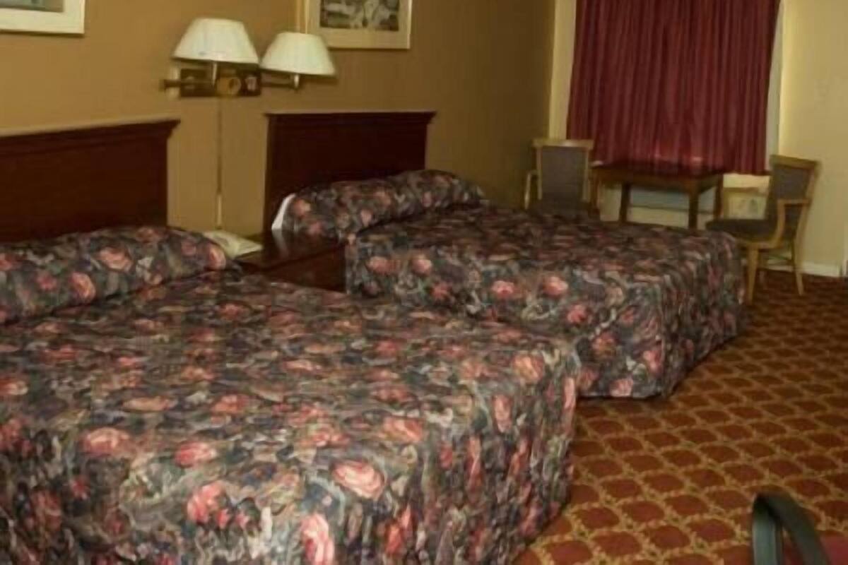 A hotel room with two beds, a desk, two lamps, and a red curtain.