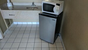A compact kitchen with a microwave on top of a refrigerator, a sink, and a tiled floor. - Budget Motor Lodge (New Castle)