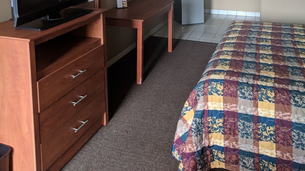 A hotel room with a wooden desk, a television, a bed with a colorful quilt, a kitchenette, and a bathroom with a mirror. - Budget Motor Lodge (New Castle)