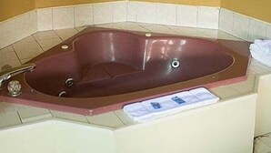 A rectangular bathtub with a control panel, set against a yellow wall with white tiles. - Budget Motor Lodge (New Castle)