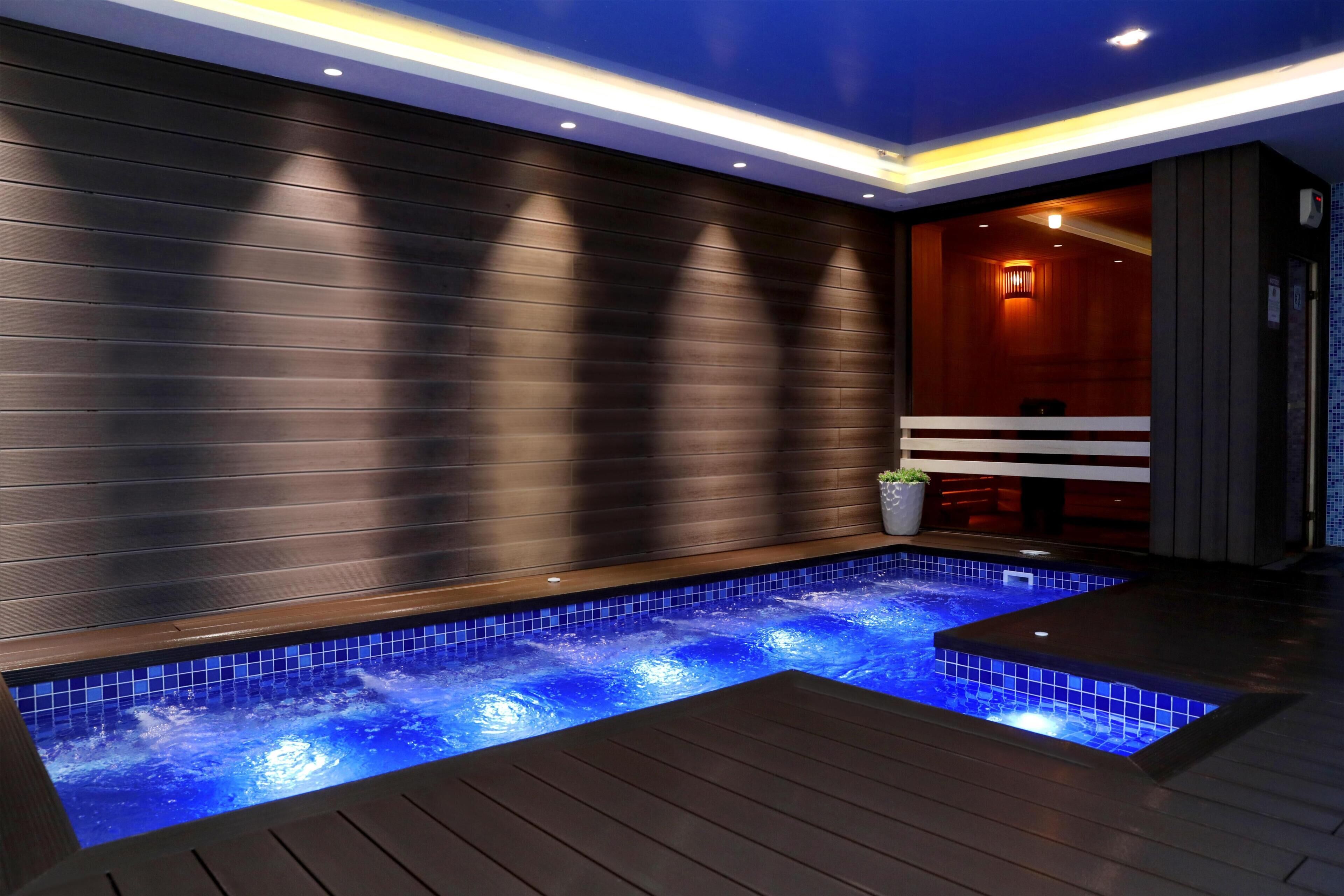 Un moderno espacio de spa con piscina climatizada, suelo de madera y una pared con paneles horizontales.