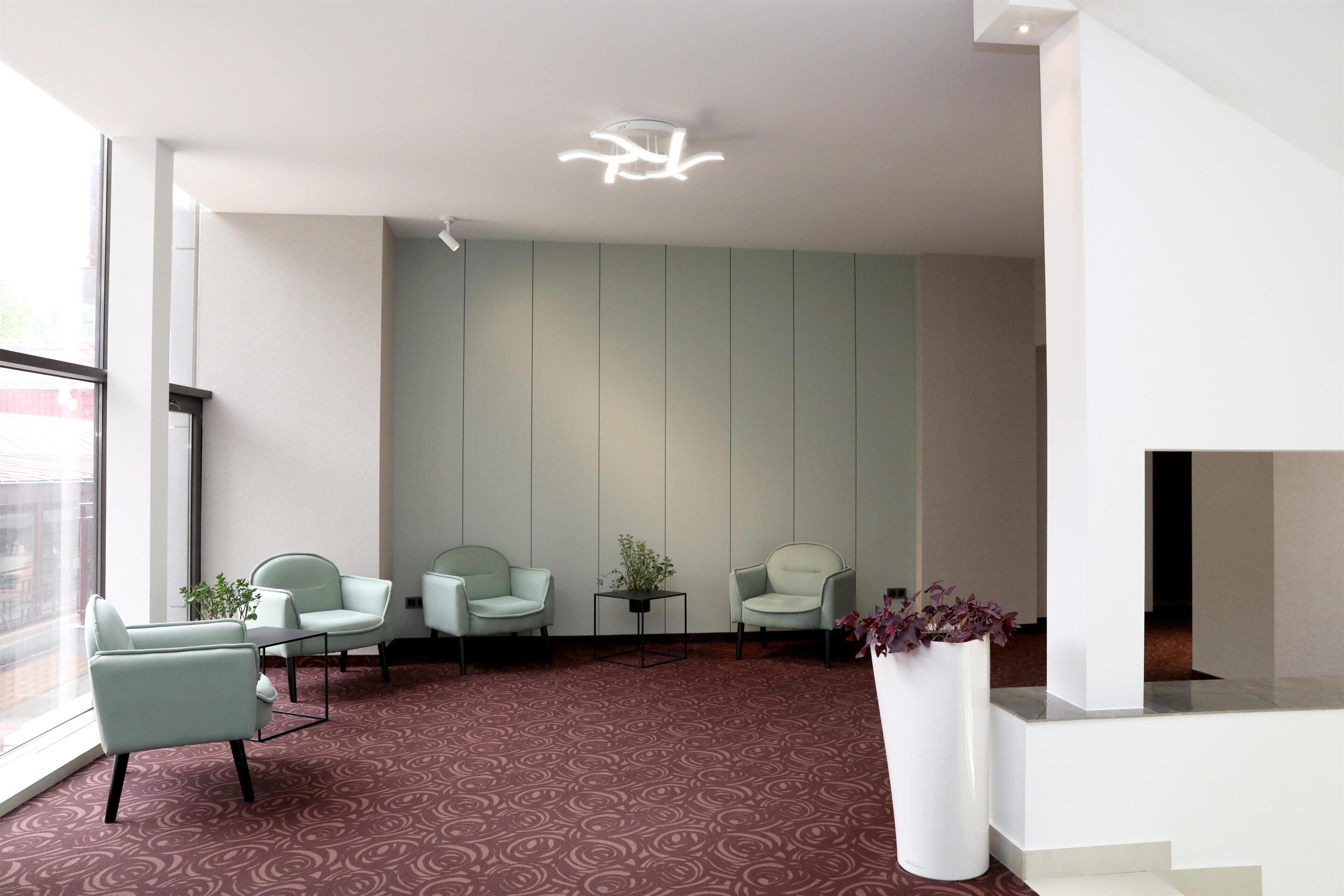 A modern waiting area with a patterned carpet, three light-colored chairs, a small table, and a potted plant.
