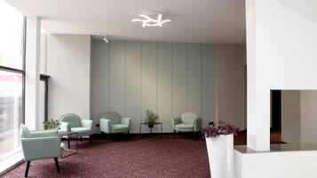 A modern waiting area with a patterned carpet, three light-colored chairs, a small table, and a potted plant.