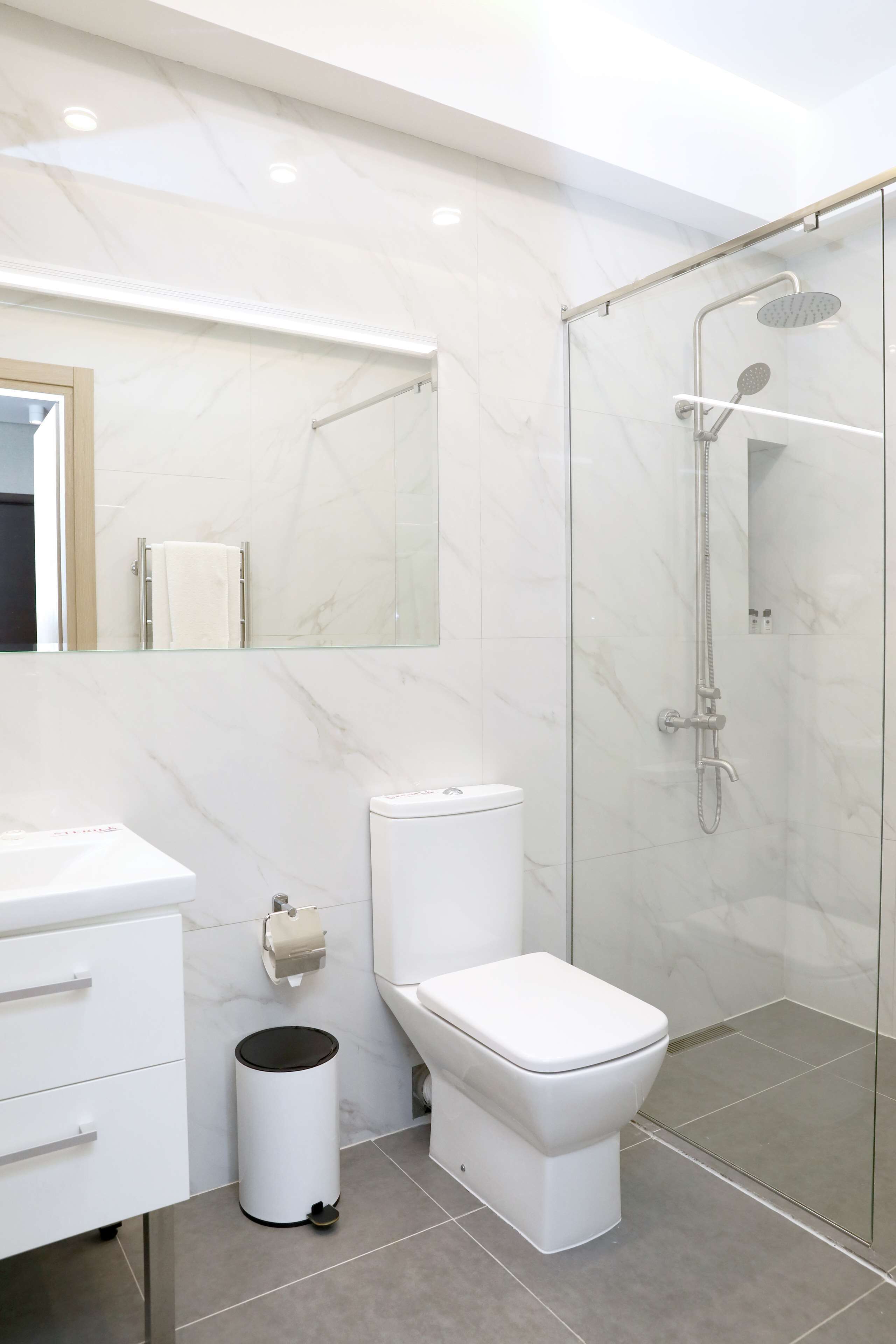 A modern bathroom with a glass-enclosed shower, a white toilet, a white sink, and a trash bin.