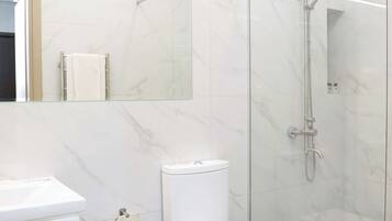 A modern bathroom with a glass-enclosed shower, a white toilet, a white sink, and a trash bin.