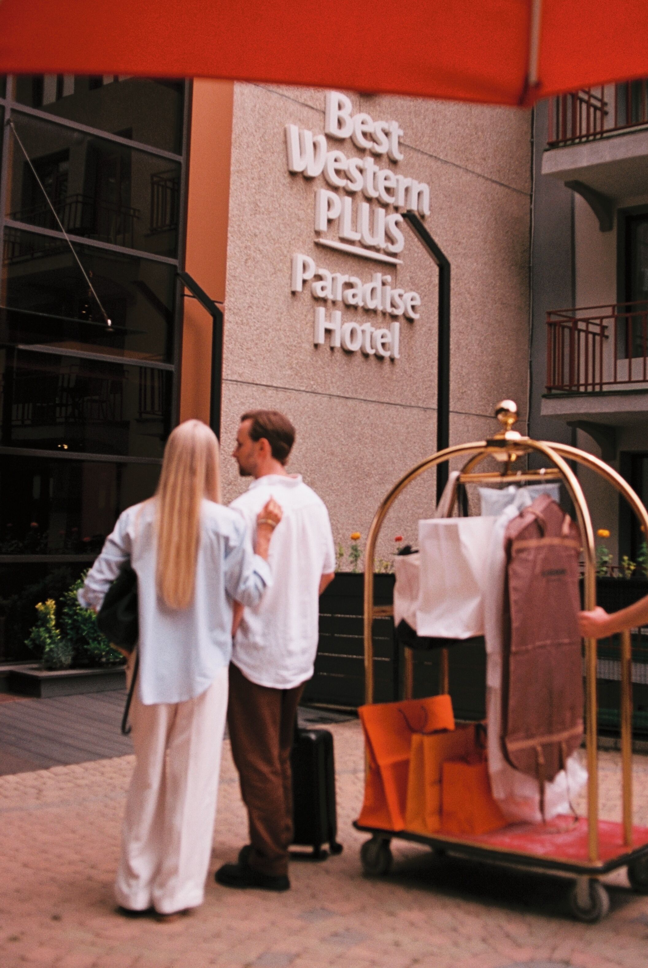 A couple standing in front of a building with a sign that reads 'Best Western PLUS Paradise Hotel.'