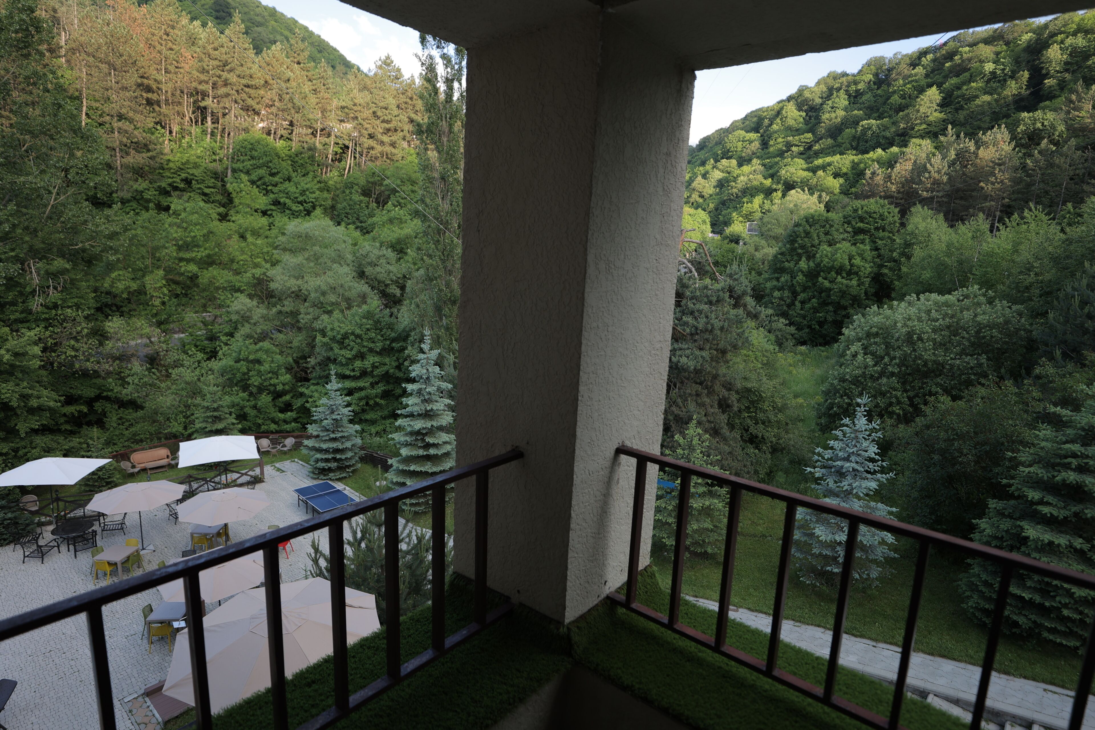 A balcony with a view of a forested area, outdoor furniture, and a paved patio.