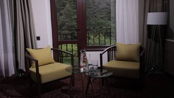 A room with two armchairs, a glass table, a pitcher, and a view of a forest through a window.
