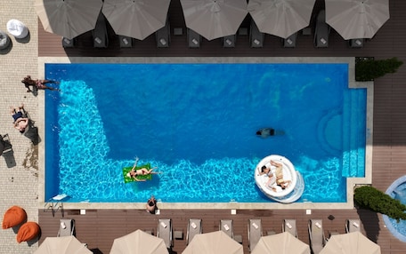 A rectangular swimming pool with lounge chairs and umbrellas around it.