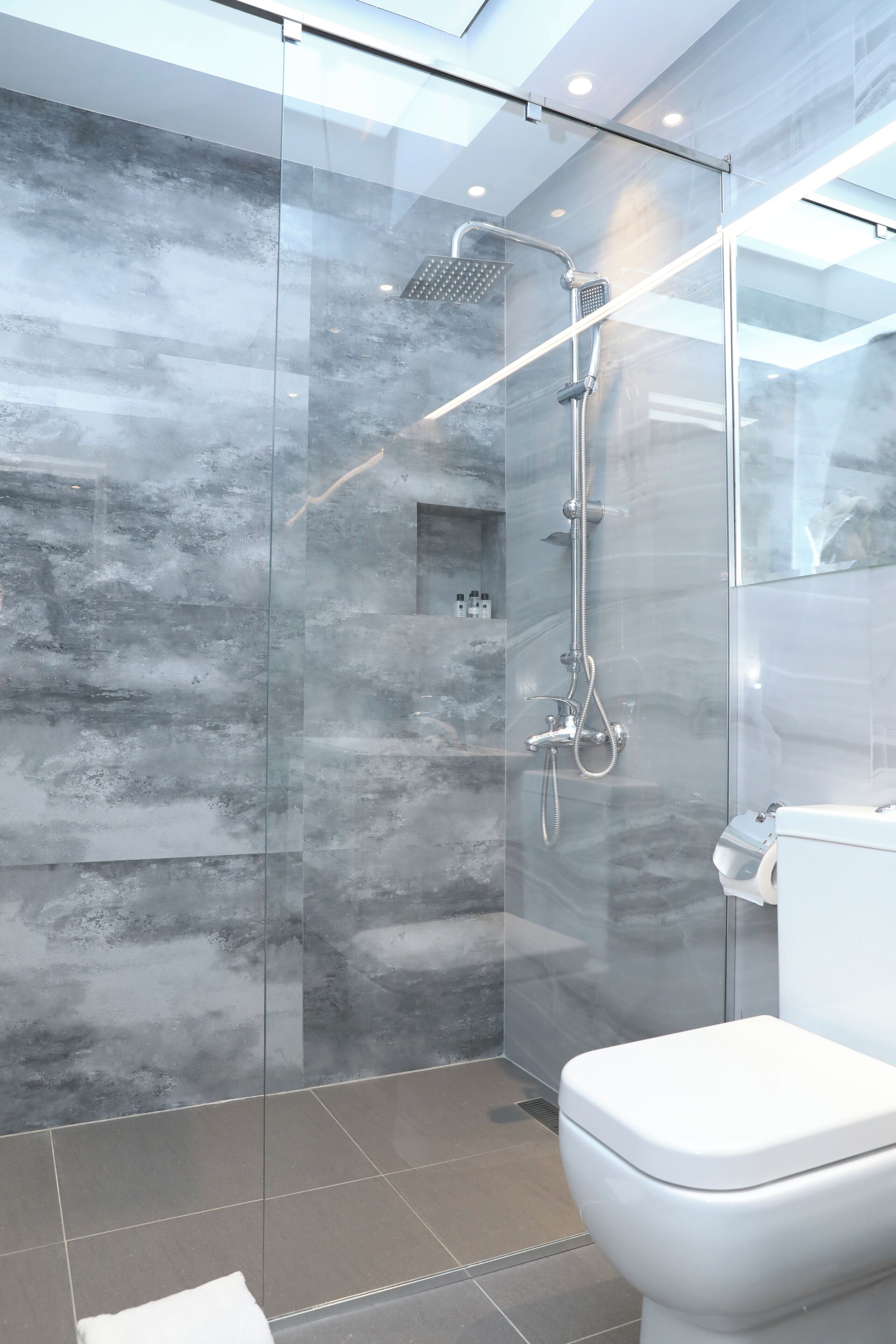 A modern bathroom with a glass-enclosed shower, a toilet, and a marble backsplash.