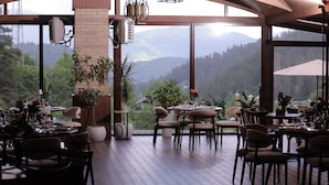 Un espace de restauration intérieur doté de nombreuses tables et chaises, et de grandes fenêtres offrant une vue sur les montagnes et la verdure.