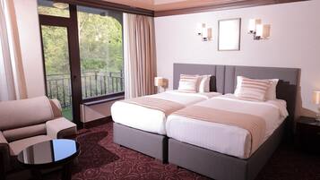 A hotel room with a double bed, a chair, a small table, and a balcony with curtains.