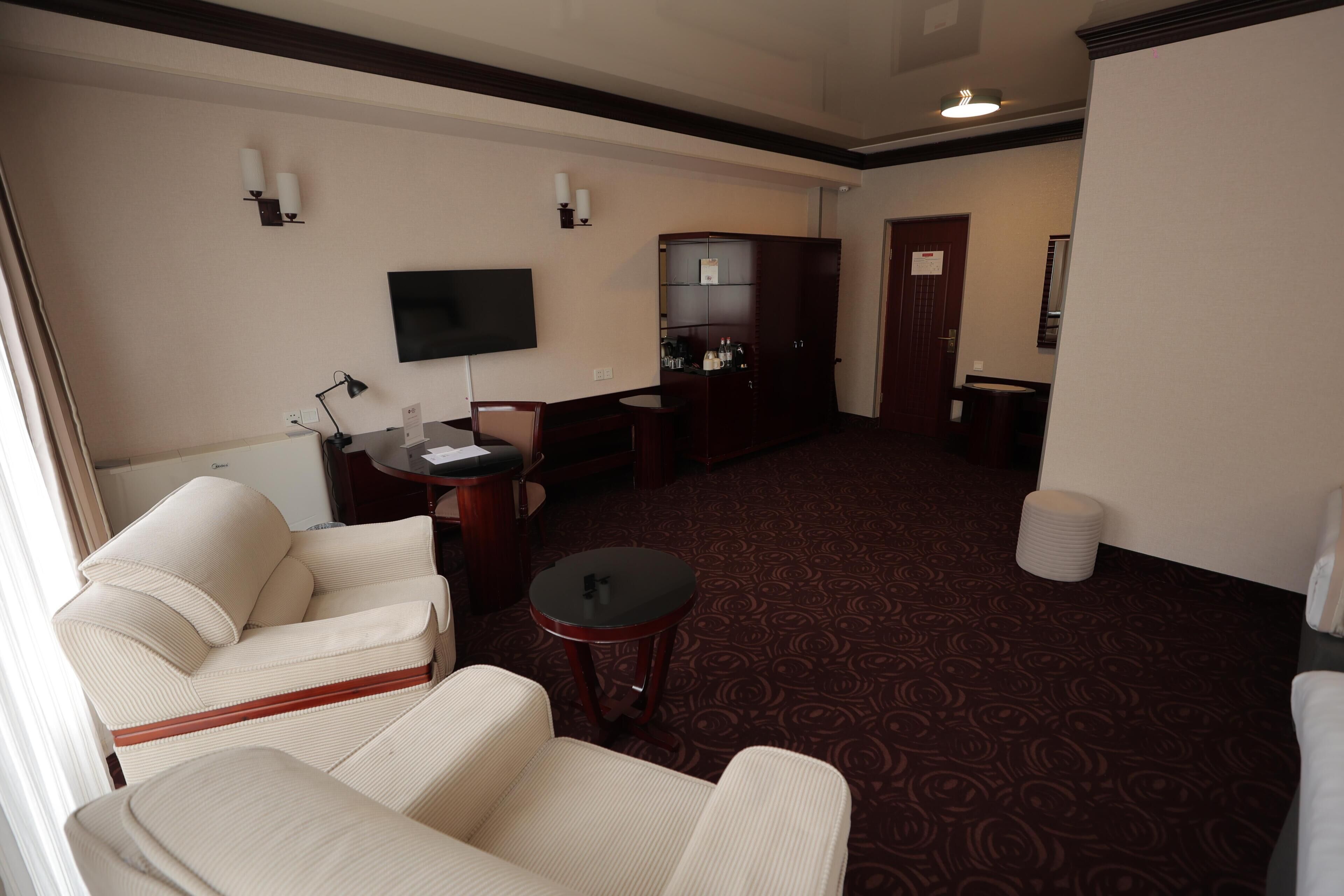 Une chambre d’hôtel avec un canapé, une petite table ronde, un téléviseur, un minibar et une moquette à motifs.
