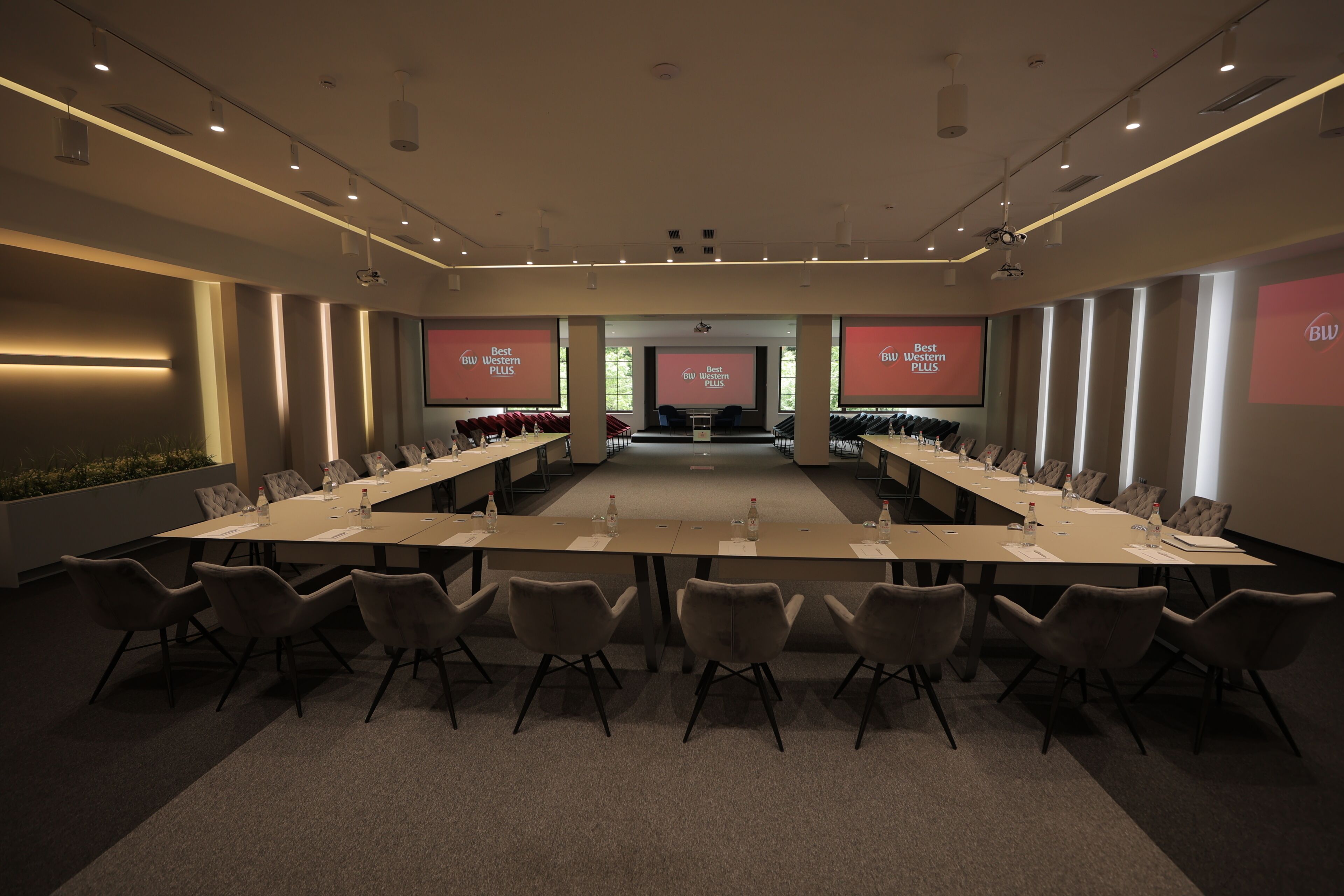 Un salón de conferencias con una larga mesa, sillas y una pantalla mostrando texto.