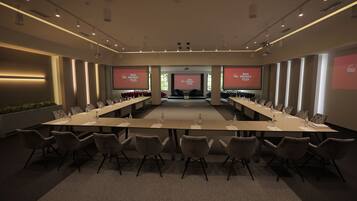 Un salón de conferencias con una larga mesa, sillas y una pantalla mostrando texto.