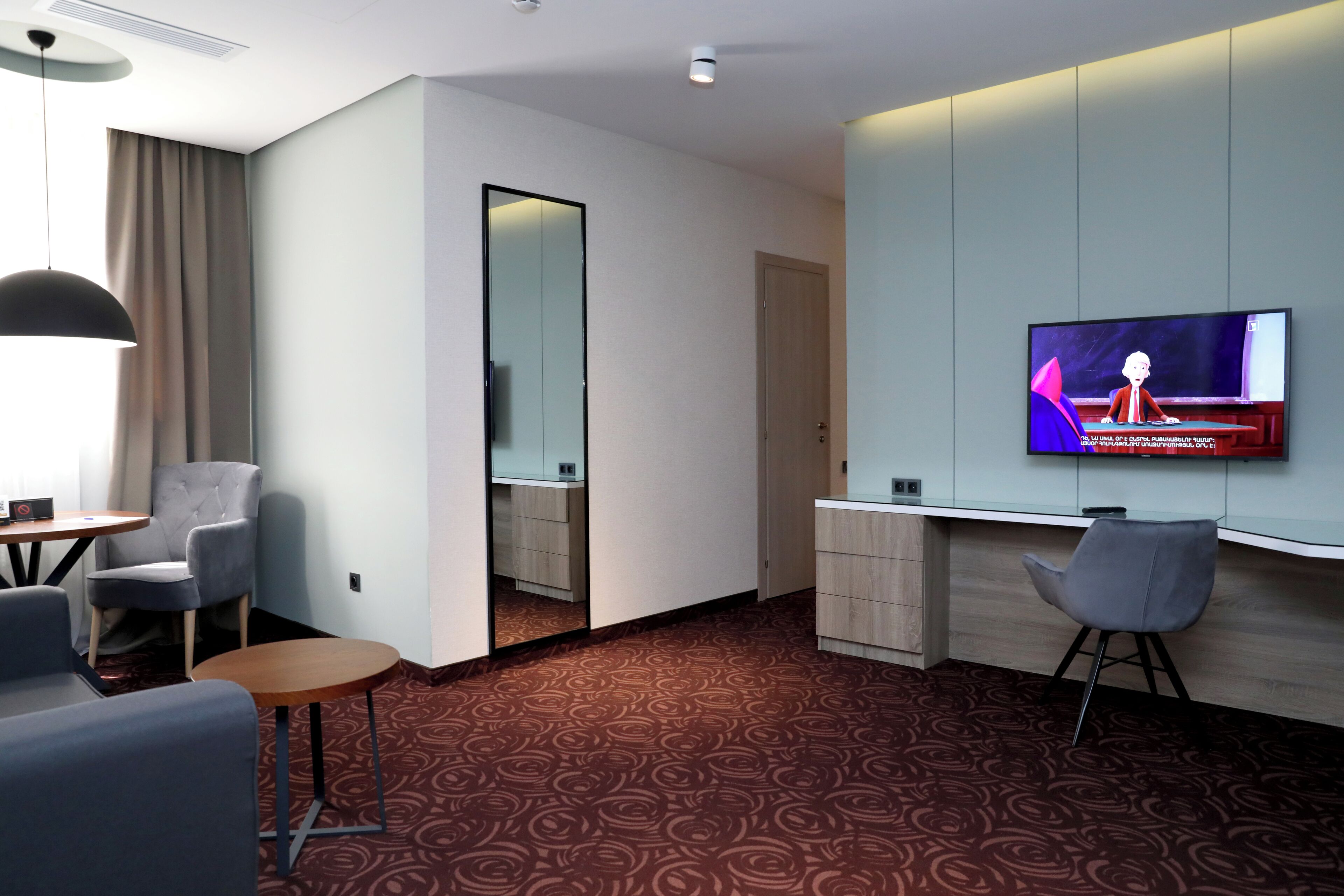 A modern hotel room with a TV, seating area, and a mirror.