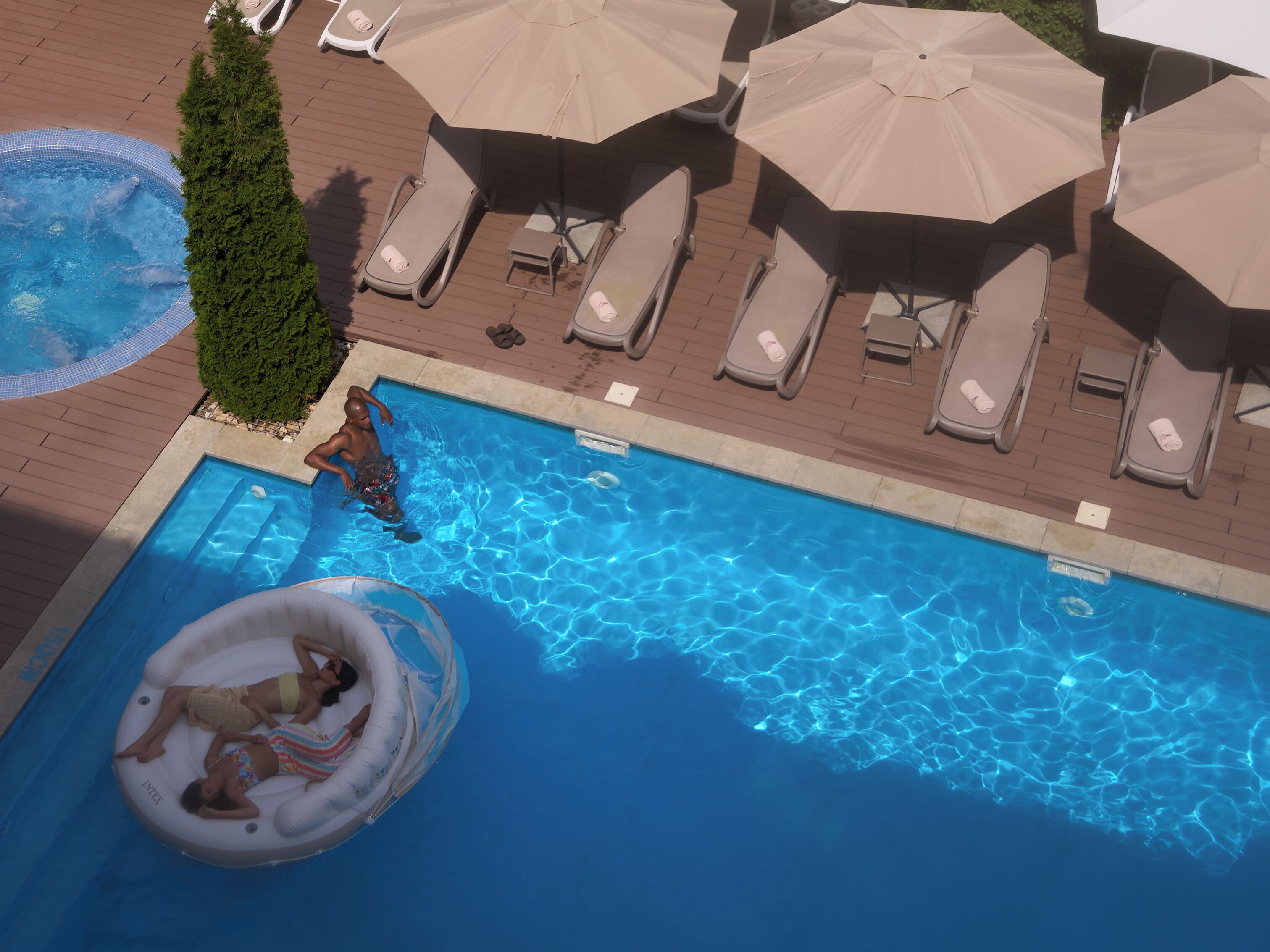 Una piscina con lettini e ombrelloni, circondata da un solarium in legno.