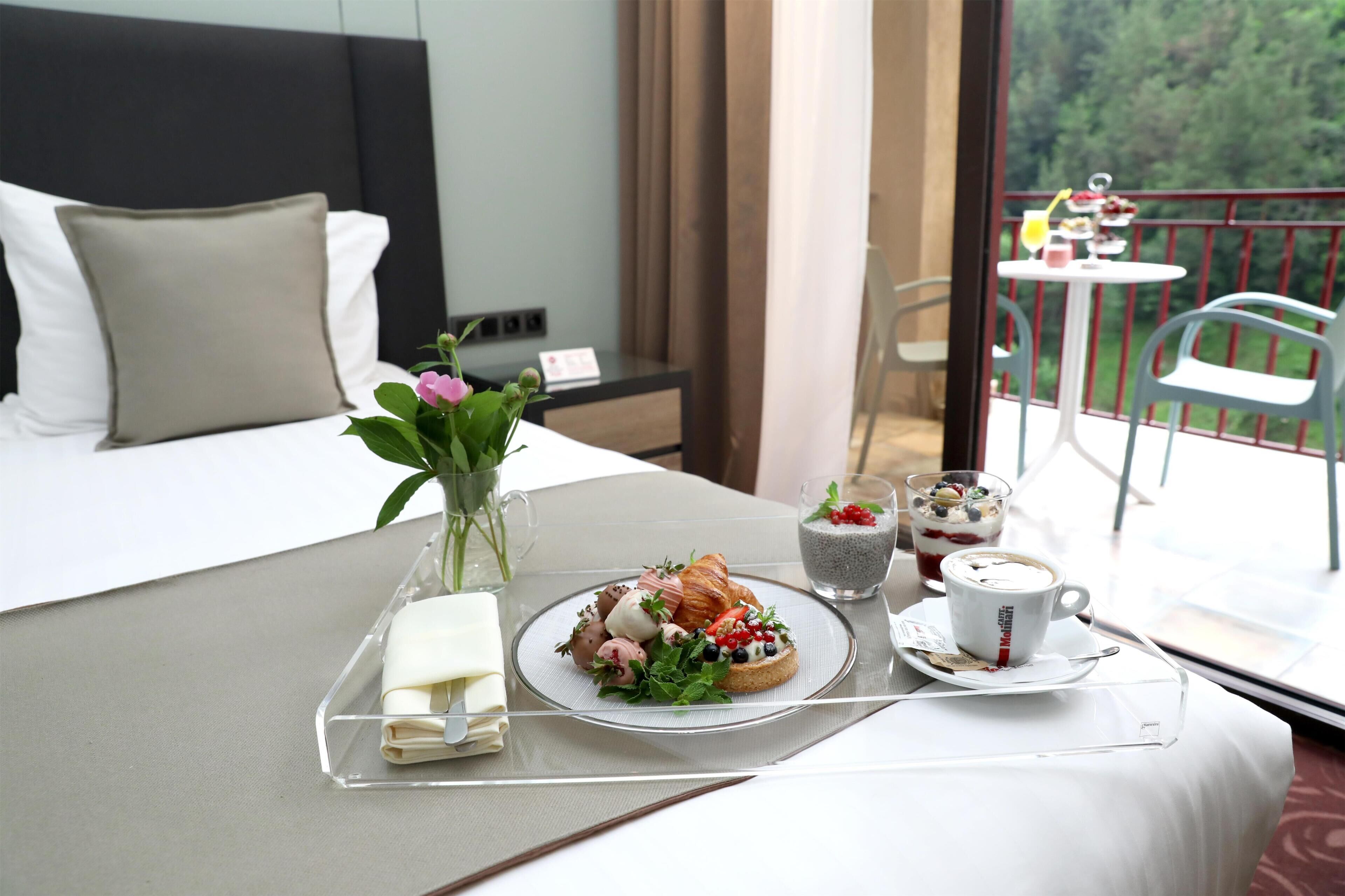 A hotel room with a bed, a breakfast tray with croissants, berries, and a cup of coffee.